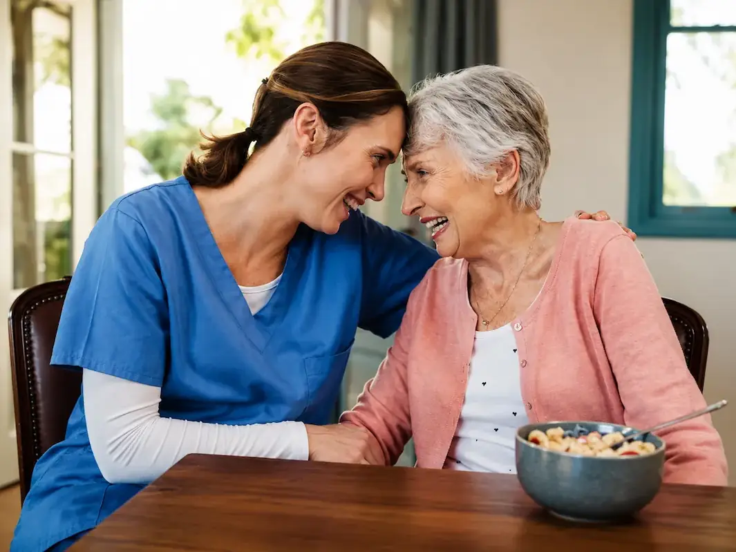 A caregiver and a senior woman laughing together at the table